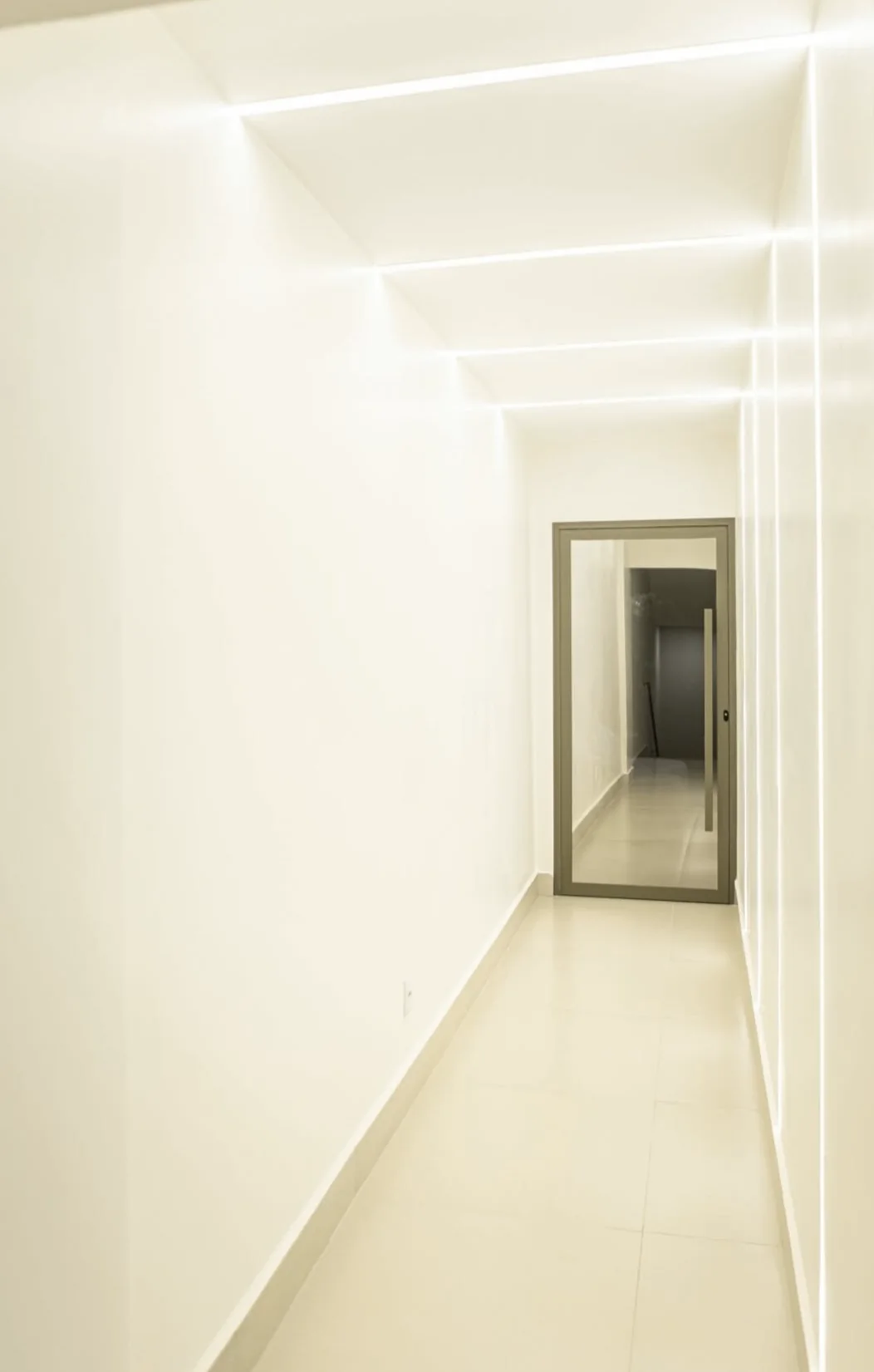 Corredor branco do Instituto Harmonizare, com linhas de luz no teto e na parede levando a uma porta ao fundo