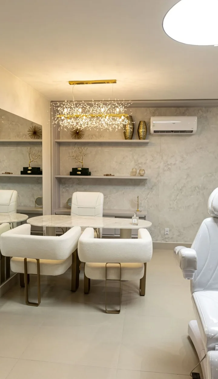 Consultório com mesa de mármore, duas poltronas claras e lustre de fios de luz