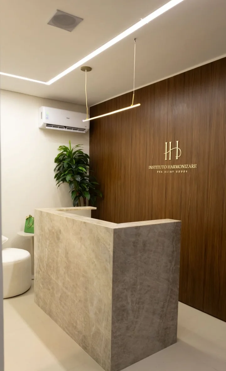 Recepção do Instituto Harmonizare: balcão de quartzito e painel de nogueira com o nome do instituto em latão